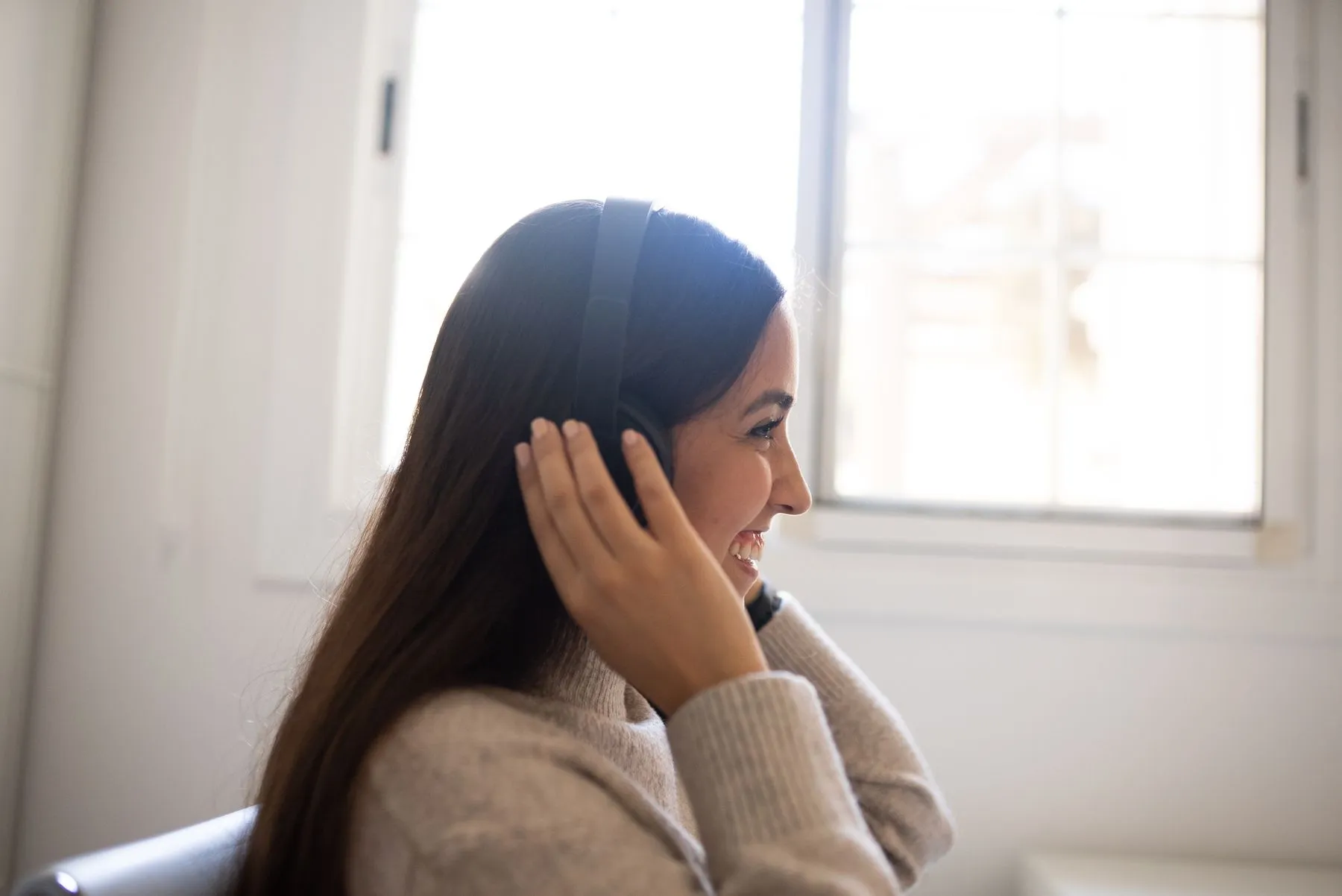 A woman in headphones by a bright window, eyes half-closed and smiling