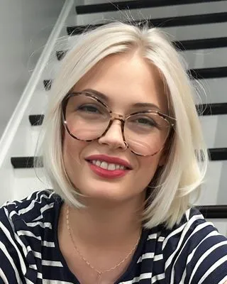 Chrissy Gallo-Nizic, smiling, with shoulder-length platinum hair and tortoiseshell glasses