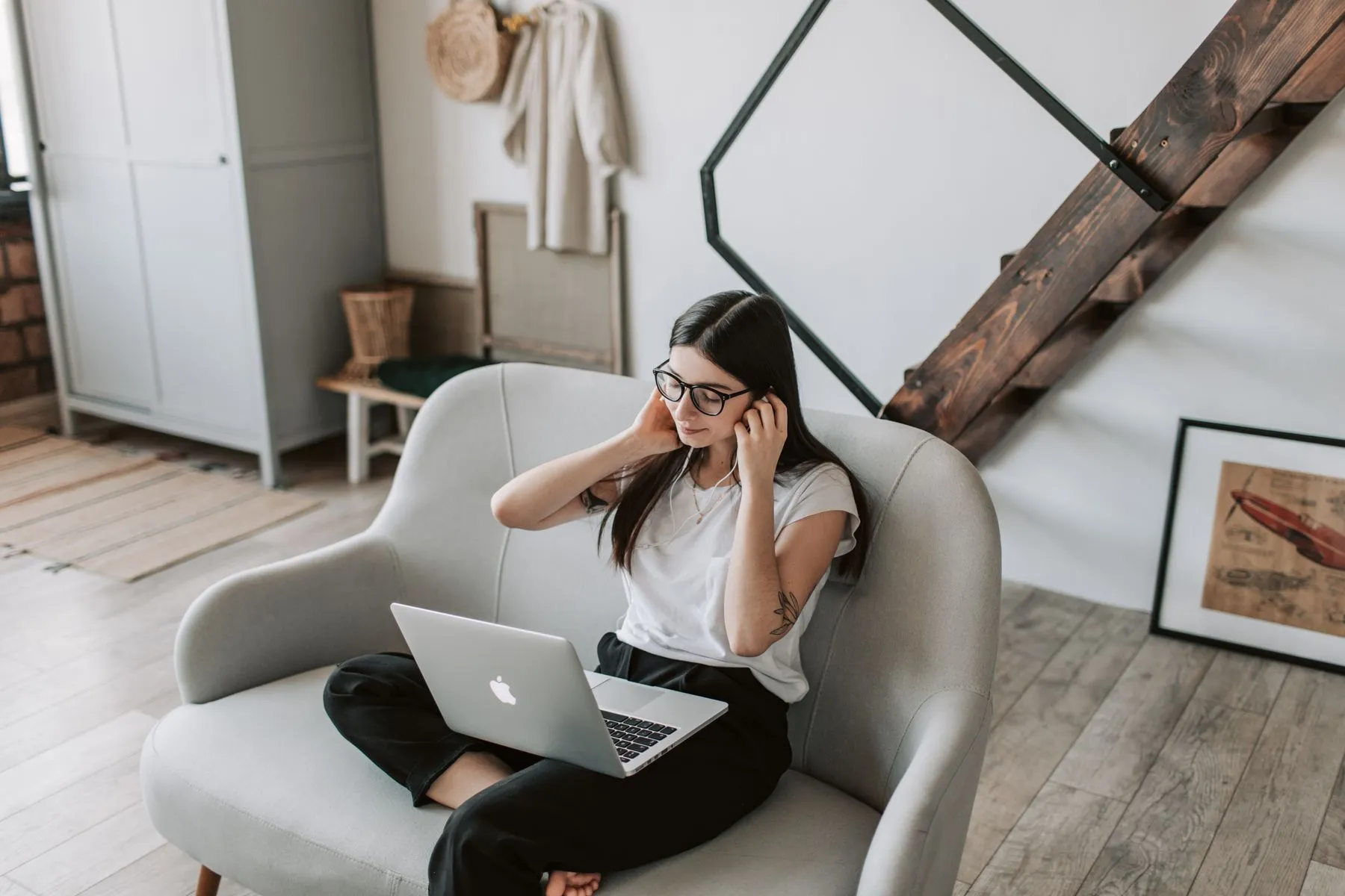 A woman in an armchair at home with a laptop and earbuds